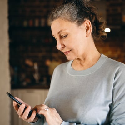 Middle-age woman in grey sweater looks down at phone