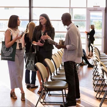 Men-and-women-stand-in-large-room-with-chairs-after-town-hall-meeting
