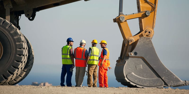 Construction works and public works inspector stand on construction site with backhoe 