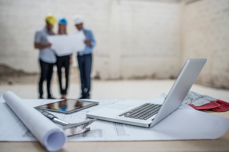 laptop and blueprints with group standing in background
