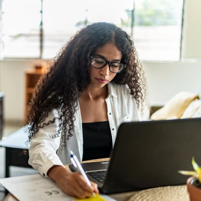 employee-looking-at-spreadsheet-on-laptop-and-taking-notes