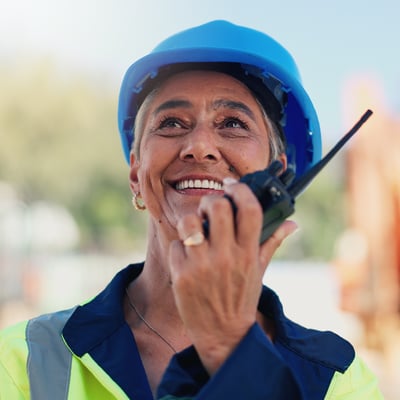 Smiling woman uses a radio at a worksite. 