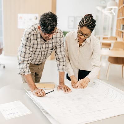 two-people-reviewing-plans-at-desk